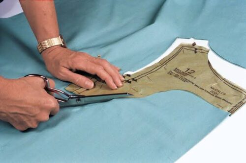 A seamstress cutting out a paper pattern from light blue gabardine.